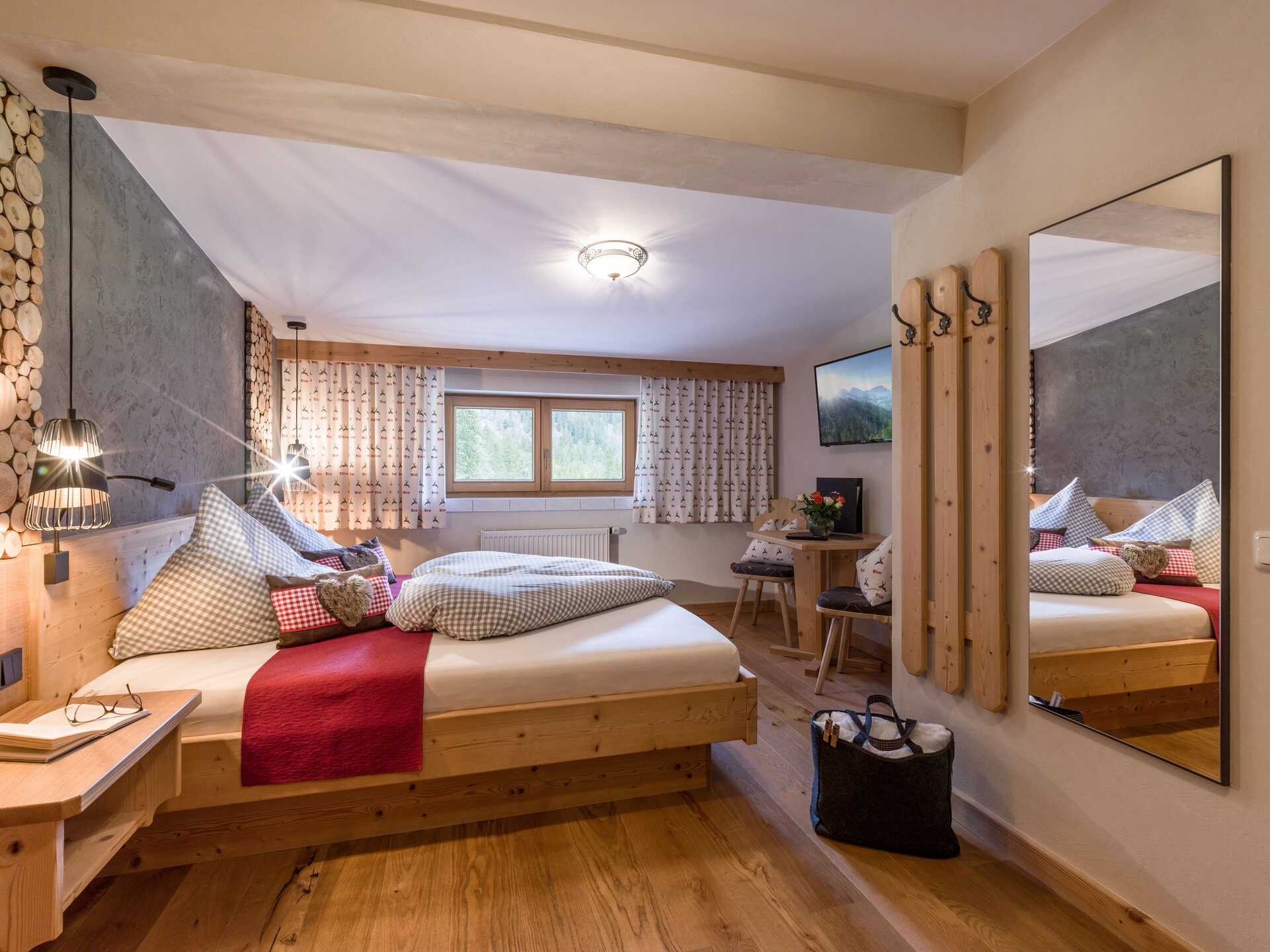 Gemütliches Alpenzimmer mit Holzboden, großem Bett, rustikalen Vorhängen, Garderobe und Panoramafenster.